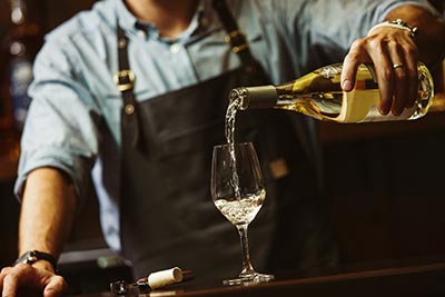 male sommelier pouring white wine into long stemmed wineglasses.